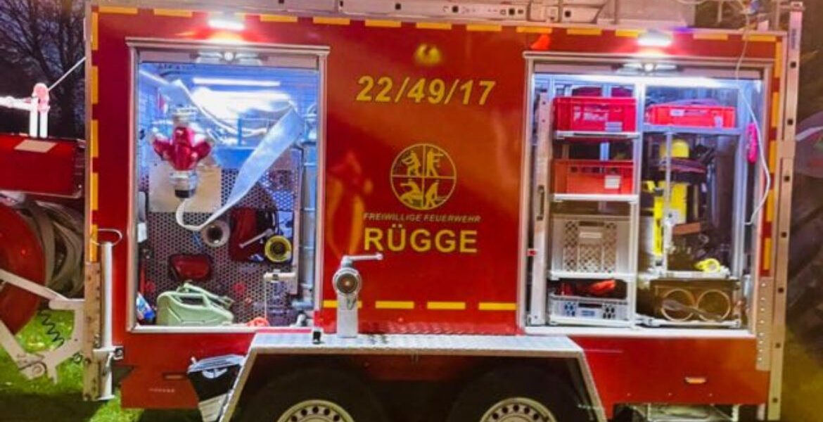 Roter Tragkraftspritzenanhänger der Feuerwehr Rügge in der Dämmerung mit geöffneten, beleuchteten Geräteräumen