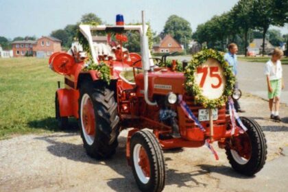 Geschmückter roter Traktor mit Tragkraftspritze und einem Schild mit der Zahl 75 vor einer Dorfstraße